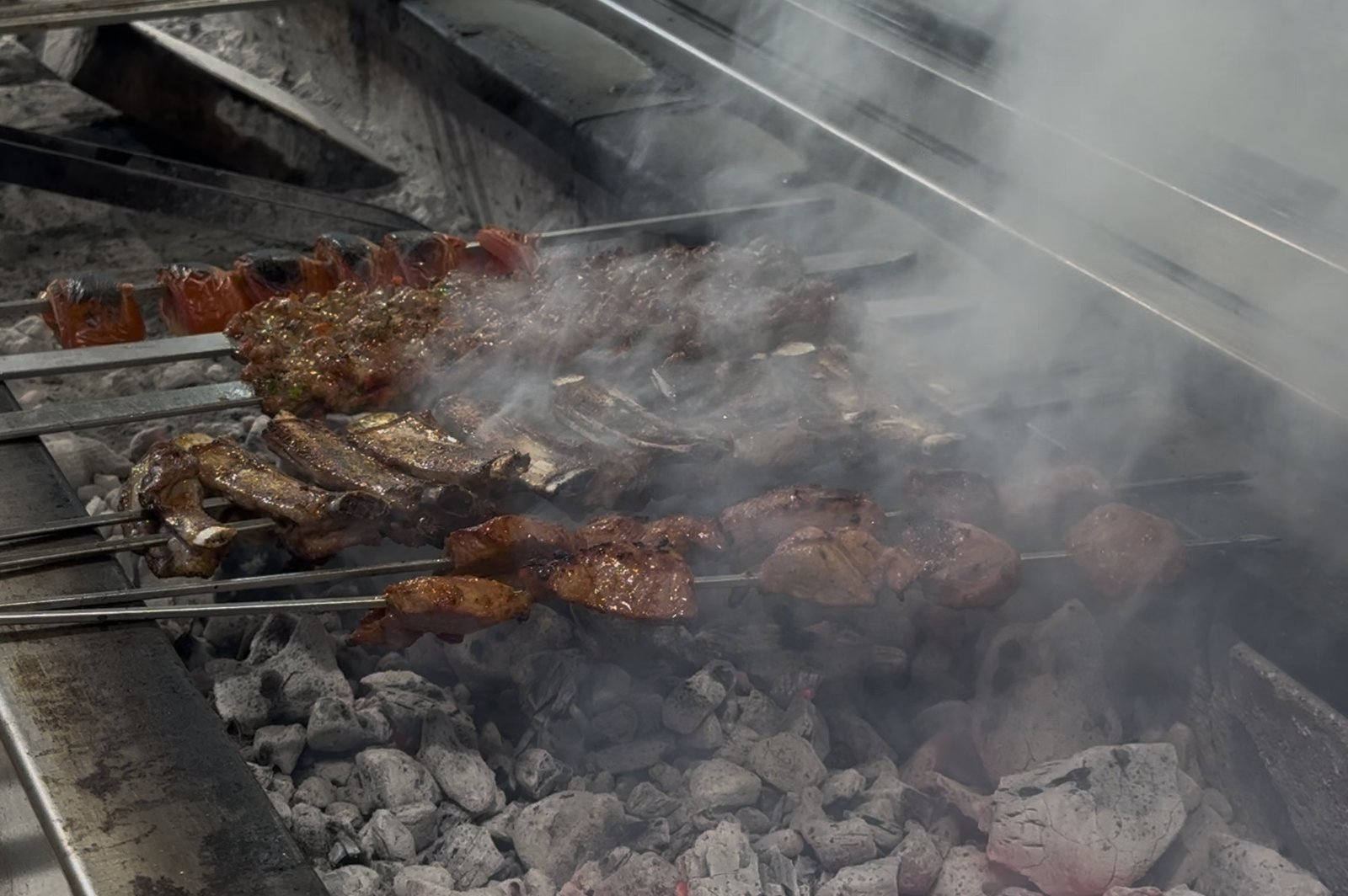 Skewers cooking on the long charcoal mangal at Kelebek Ocakbaşı, steam rising
